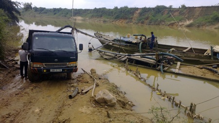 Một cát tặc chuẩn bị ống hút để bơm cát từ thuyền lên xe