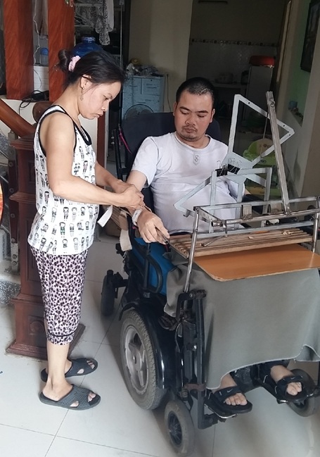 Người thầy ngồi xe lăn chắp cánh cho hàng trăm học trò đỗ đại học - 2 Vợ thầy Huấn đang giúp chồng gắn bút vào cổ tay
