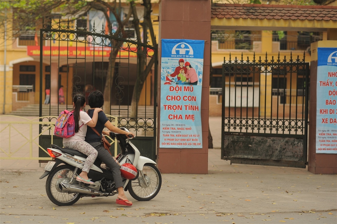 Ngay cổng trường có băng rôn tuyên truyền đội mũ cho trẻ em nhưng các bậc phụ huynh vẫn phớt lờ