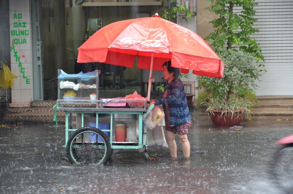 Một người bán hàng rong đẩy xe trong dòng nước đen ngòm
