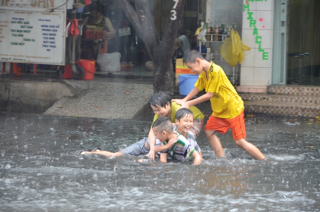 Nhiều em nhỏ tắm mưa trên đường ngập.