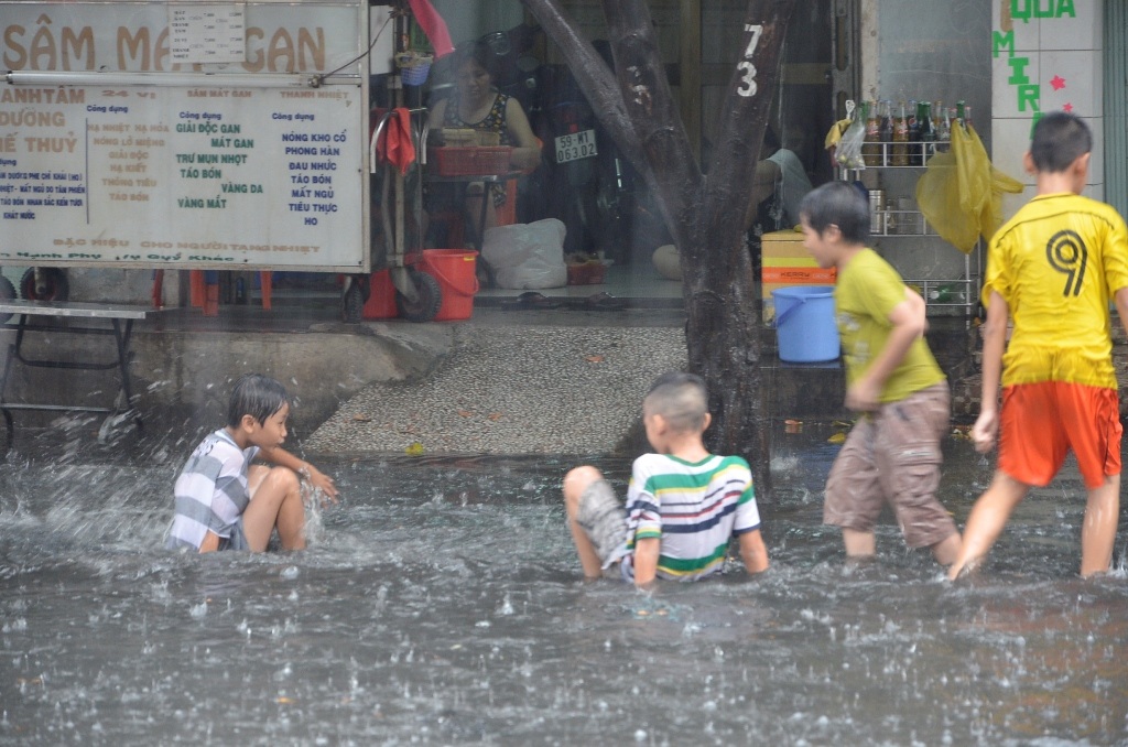 Nhiều em nhỏ tắm mưa trên đường ngập.
