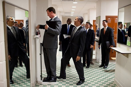 Tổng thống Obama và nghệ sĩ Mỹ: Những ân tình trong suốt 8 năm - 6 Ông Obama đặt chân của mình lên cân trong khi một người nhân viên đang tranh thủ kiểm tra cân nặng. Trò đùa của ông đã được nhiếp ảnh gia nhanh chóng ghi lại. Bức ảnh này cũng giống như rất nhiều bức ảnh khác xuất hiện ở đây đã từng gây sốt trên các mặt báo, giúp người ta hiểu hơn về cá tính và cuộc sống thường nhật của ông Obama.