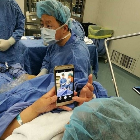 Thú vị cảnh nữ bệnh nhân chơi smartphone để... giảm đau - 1 Bà Zhu bình thản sử dụng smartphone trong khi các bác sĩ đang thực hiện ca phẫu thuật cho mình