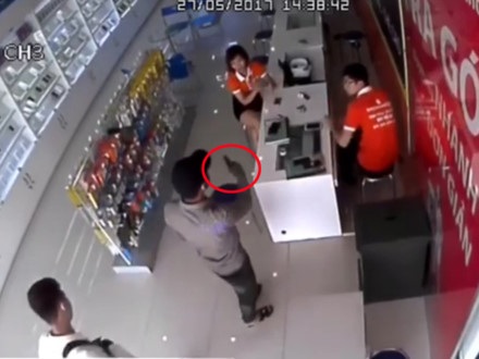 
Một thanh niên mang súng (trong vòng đỏ) đe dọa nhân viên. Ảnh cắt từ clip (nguồn: Lao động)
