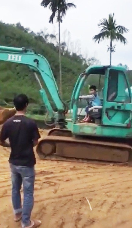 
Cậu bé điều khiển xe múc trước sự chứng kiến của người lớn.
