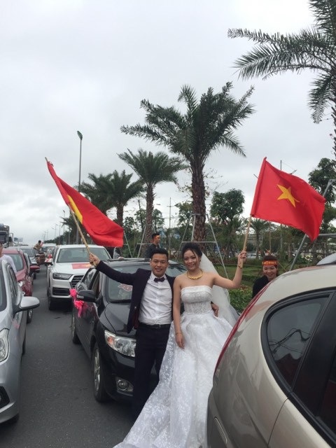 Hình ảnh cặp đôi vẫn trong trang phục lễ cưới, cầm cờ đỏ sao vàng “cháy” hết mình cổ vũ các cầu thủ lập tức gây “sốt” trên khắp các diễn đàn.
