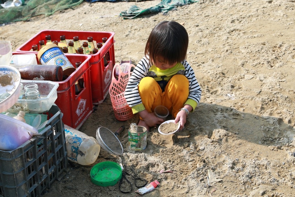 Ở nơi Tết cũng như... ngày thường! - 5 Một em bé hồn nhiên ngồi trên bờ chơi đùa để bố mẹ dọn dẹp. Không khí Tết đã cận kề nhưng tại đây dường như những gì liên quan tới sắm sửa, đồ mới, thức ăn, kẹo mứt vẫn thiếu thốn