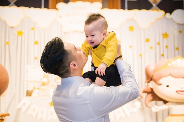 Cậu nhóc ngoan ngoãn khi được bố bế đi chào hỏi quan khách.