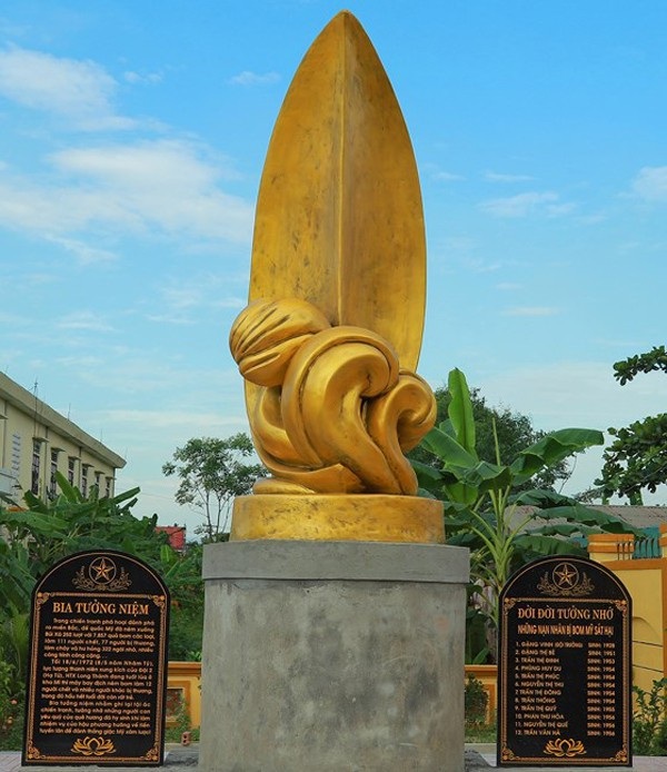Khánh thành Bia tưởng niệm 12 nạn nhân chết trong trận bom kho Mí - 1 Bia tưởng niệm với biểu tượng lá lúa đặt trên 1/2 quả bom cắm xuống đất đặt giữa 2 bia ghi tên những nạn nhân bị trận bom năm 1972