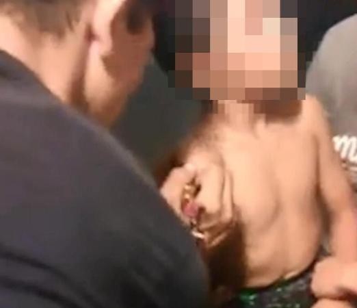 Trong video, bé trai được người thanh niên xăm một chữ “S” lớn trên cánh tay phải