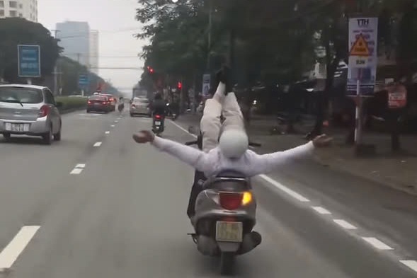 Người đàn ông nằm giơ cả 2 tay 2 chân trên xe máy đang chạy