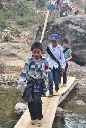 Học sinh địa phương đi trên chiếc cầu gỗ vừa mới được bắc tạm qua con suối tang thương