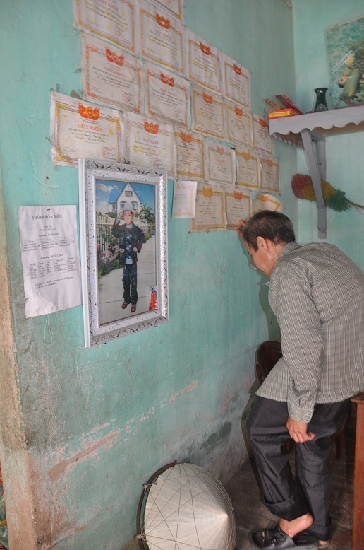 Bên cạnh người chồng còng rạp đứng xót xa cố nhìn những tờ giấy khen của các con.