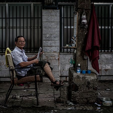 Ông Binh, 60 tuổi, vừa đọc báo vừa hút thuốc trong lúc vắng khách.