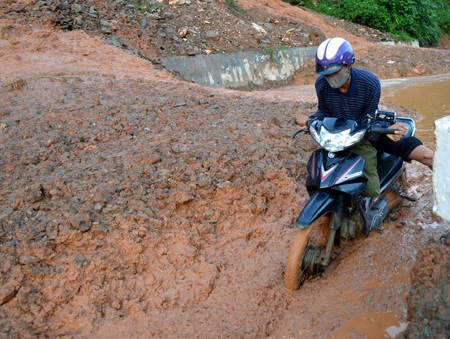 Một người cố gắng dắt xe máy qua điểm sạt lở nhưng không được nên phải huy động người bưng.