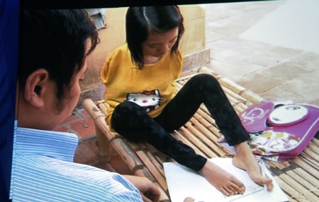 Thầy Tuấn hướng dẫn em Lê Thị Thắm cụt hai tay viết bằng chân.