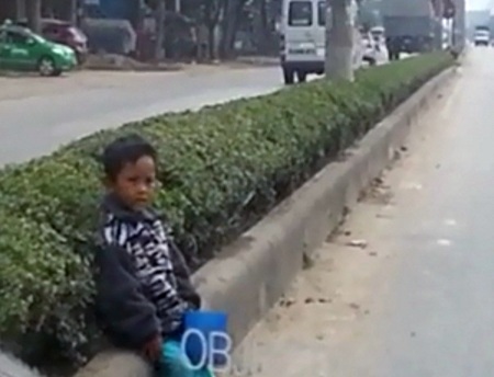 Mệt quá cháu bé ngồi xuống dải phân cách đường để nghỉ.