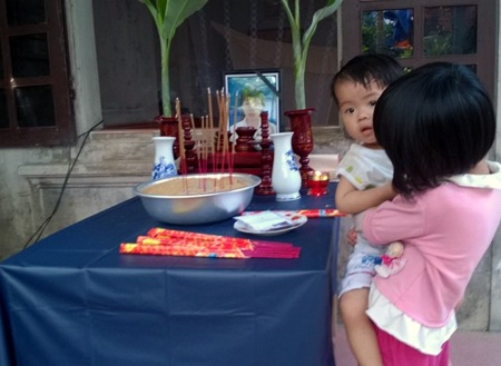 Cháu Quỳnh Chi bế em 18 tháng tuổi bên bàn thờ mẹ. 