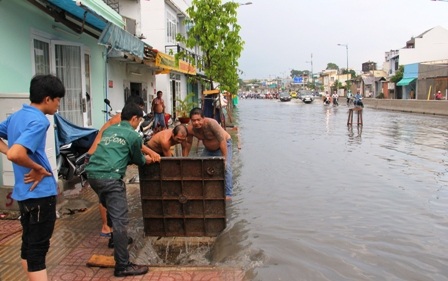 Nhiều người cùng nhau dùng xà beng cạy nắp cống trên đường Phạm Văn Đồng để nước thoát.