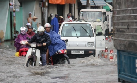 Nhiều người cùng nhau dùng xà beng cạy nắp cống trên đường Phạm Văn Đồng để nước thoát.