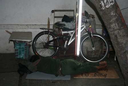 Người đánh bóng lư đồng tự xích tay mình vào chiếc xe đạp trên vỉa hè