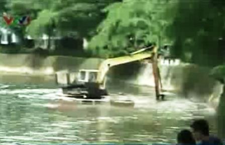 Nạo vét bùn dưới sông rồi lại đổ... xuống sông - 1 Xe xúc nạo bùn ở bờ sông (ảnh chụp từ clip của VTV)