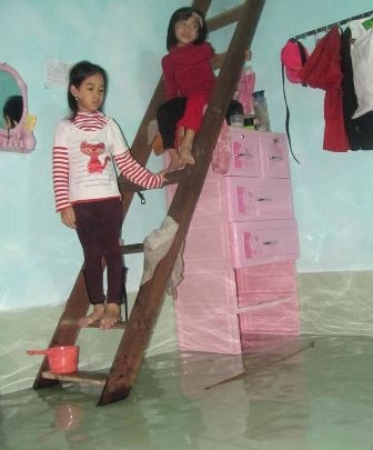 Lũ lên quá nhanh, nhiều nơi bị nhấn chìm - 11 2 em bé đứng trên cầu thang dẫn lên gác gỗ đang chất đồ phía trên, nhìn xuống dòng nước lũ