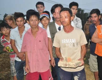 1 người dân ở đây cầm tấm bia và gạch vỡ từ mộ nhà mình cho rằng do công trình nước tăng áp gây ra