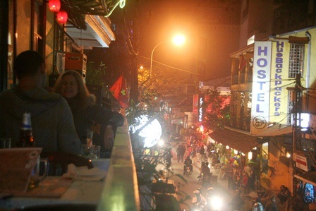 1 đôi bạn tây cười nói rôm rả từ tầng trên nhà hàng nhìn xuống khu phố Tây sầm uất