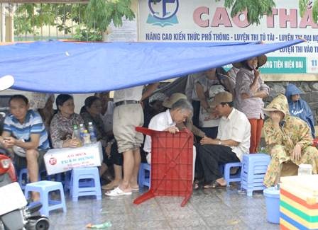 Phụ huynh ướt sũng đứng chờ con trong mưa - 2 Các phụ huynh ngồi tụm lại trong chiếc bạt nhỏ mới căng lên