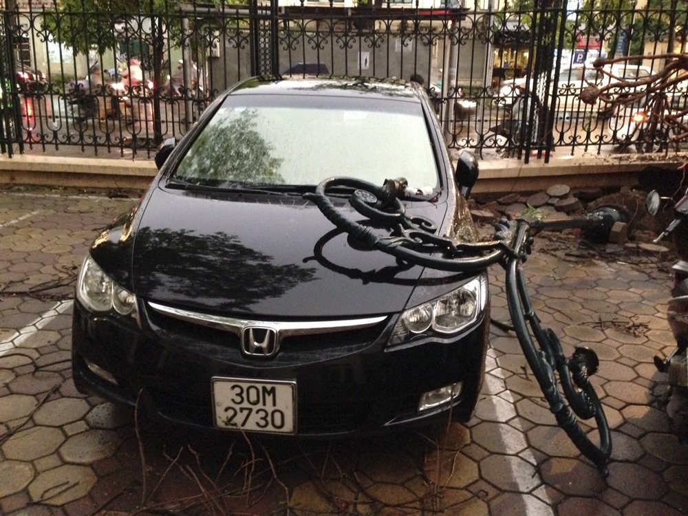 Nhiều ô tô, xe máy tan nát sau giông lốc ở Hà Nội - 5 Một cột đèn đỗ liên hoàn theo gốc cây xà cừ đè lên một chiếc ô tô khác.