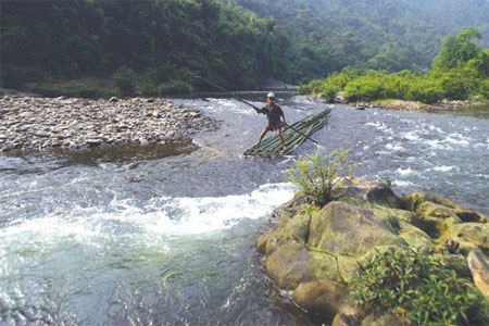 Hai người phụ nữ đang kéo những viên sỏi sát lòng sông cạn để đuổi cá vào một cái màn giăng sẵn.