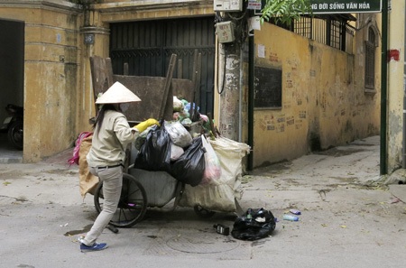 Những xe rác tự chế “đặc biệt” ở thủ đô - 3 Một công nhân môi trường vừa nhảy xuống sau khi đã leo lên đỉnh xe để lèn rác bằng chân.