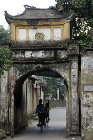 Cổng làng cổ Cự Khê với chiếc đồng hồ điện tử được treo tùy tiện phía trên lỗ hổng sát mái.