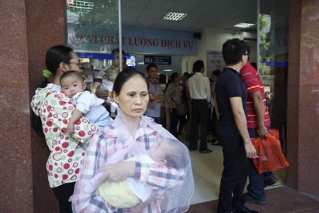 Bồng bế xếp hàng chờ tiêm phòng cho trẻ - 14 Rất nhiều người phải cho con cháu ra đứng ngoài cửa vì không khí ngột ngạt bên trong.