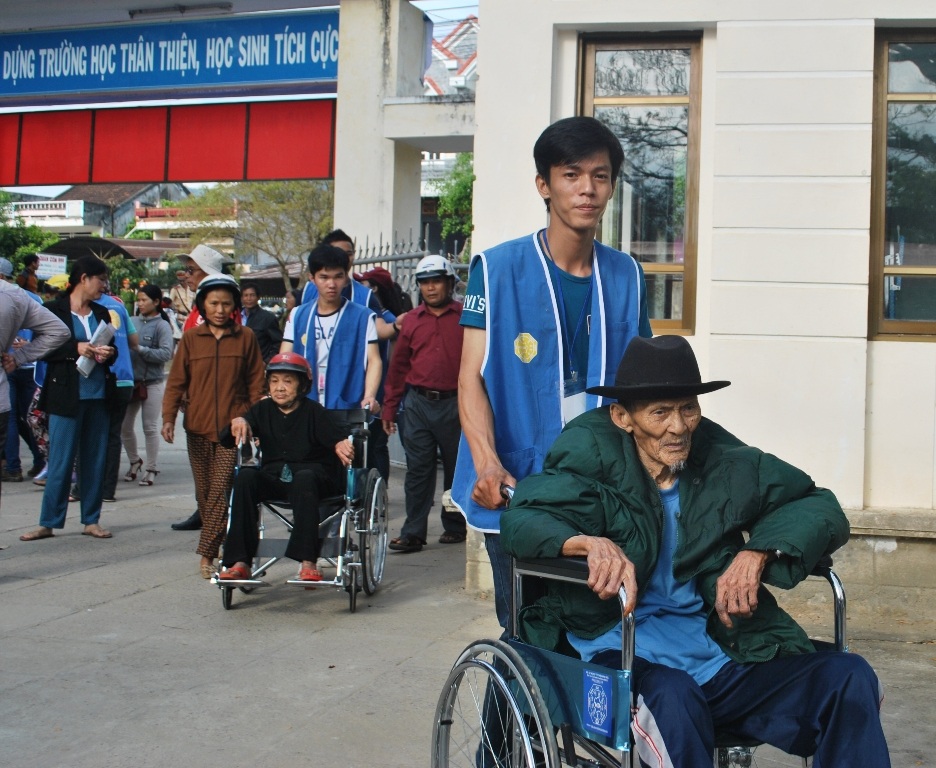 Các thiện nguyện viên giúp người già đi lại khó khăn đến khu vực khám bệnh