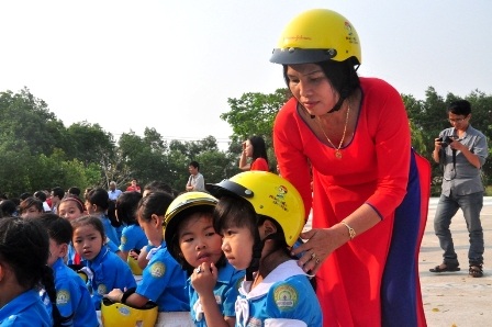 Cô giáo trường tiểu học Nguyễn Hiền giúp các em học sinh đội mũ bảo hiểm tại lễ phát động