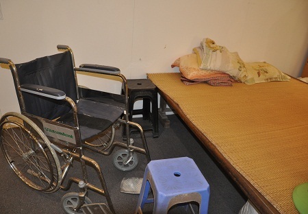Cuộc sống của những người khuyết tật được thể hiện qua chiếc xe lăn đặt cạnh chiếc giường.