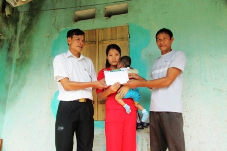 Ông Lê Văn Độ, cán bộ xã Vĩnh Ninh (trái) trao quà bạn đọc đến gia đình cháu Bảo.