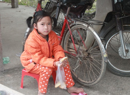 Một em bé được mẹ đưa đến chợ để trông xe, đổi lại em được mẹ mua bánh cho để đợi mẹ mua sắm.