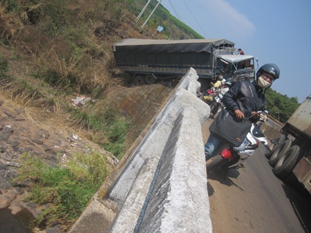 Chiếc xe phần đầu nằm trên thành cầu, một phần nằm dưới bờ suối