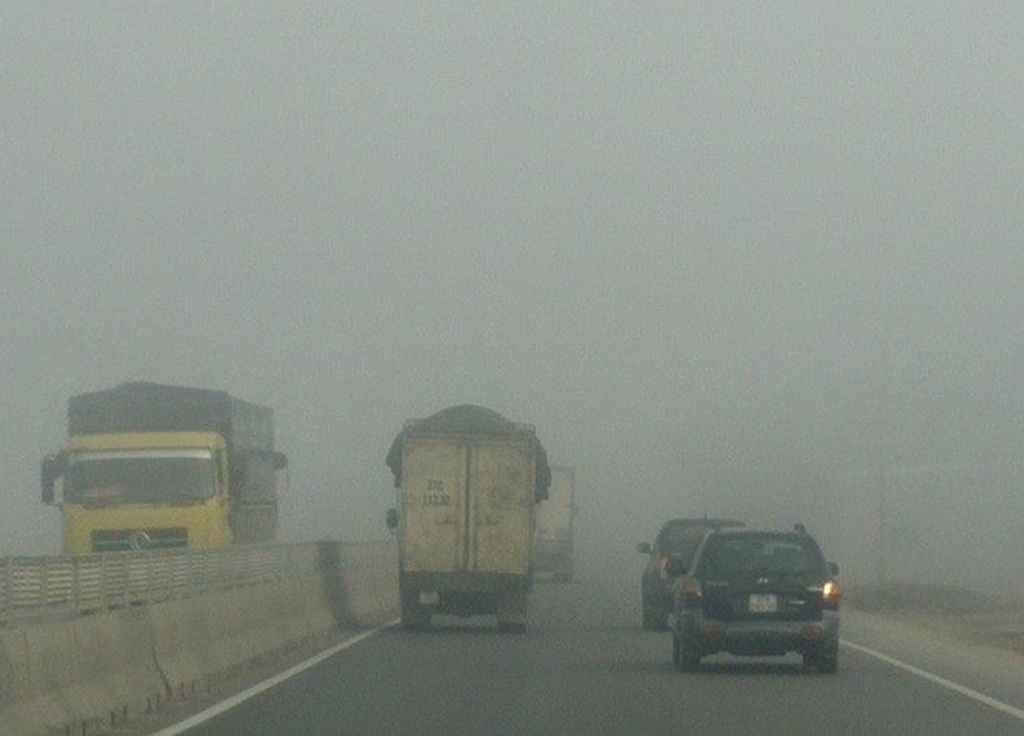 Nhiều ô tô phải bò nối đuôi nhau đi chậm trong làn sương sớm.