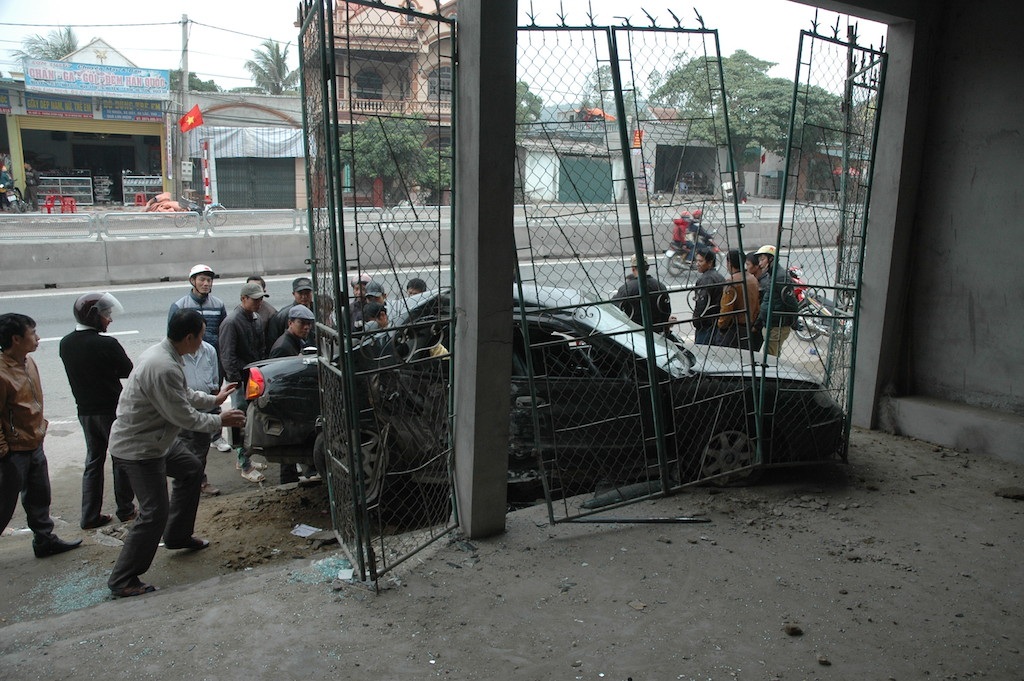 Chiếc xe con đỗ ở vỉa hè bên đường, bị xe tải đâm dồn và chiếc xe con này đâm sập cổng sắt nhà dân.