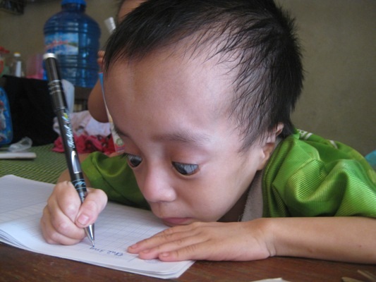 Nghị lực phi thường của cậu bé mắc bệnh não úng thủy - 2 Để viết chữ, Ngọc phải nhoài hẳn người lên bàn để viết