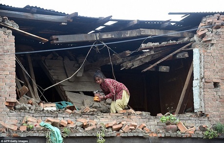 Một cô bé thu gom đồ còn sót lại tại ngôi nhà đã bị hư hại sau động đất. (Ảnh: 
