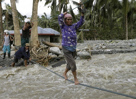 Người phụ nữ băng qua dòng nước dữ bằng những chiếc dây thừng mỏng manh. (Bullit Marquez/AP)
