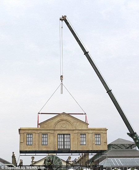 Một nửa tòa nhà đang được từ từ hạ xuống bằng cần cẩu.