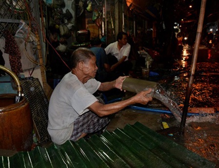 Người đàn ông ngồi tát nước ra khỏi nhà sau cơn mưa lớn