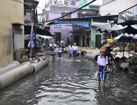 Người đàn ông ngồi tát nước ra khỏi nhà sau cơn mưa lớn